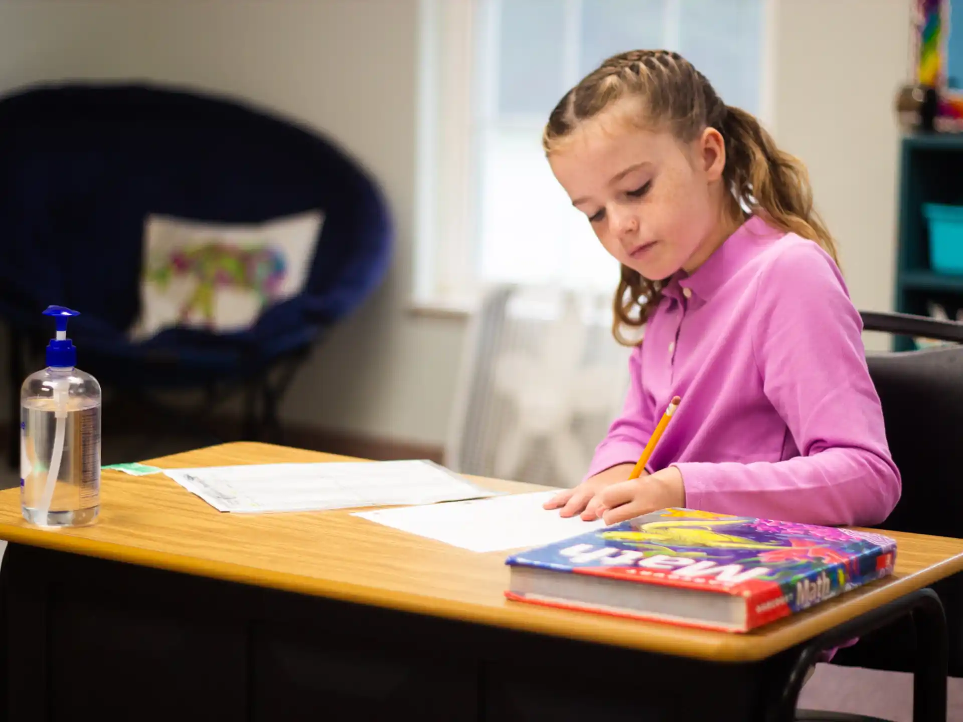 a girl sitting at a desk writing on a book