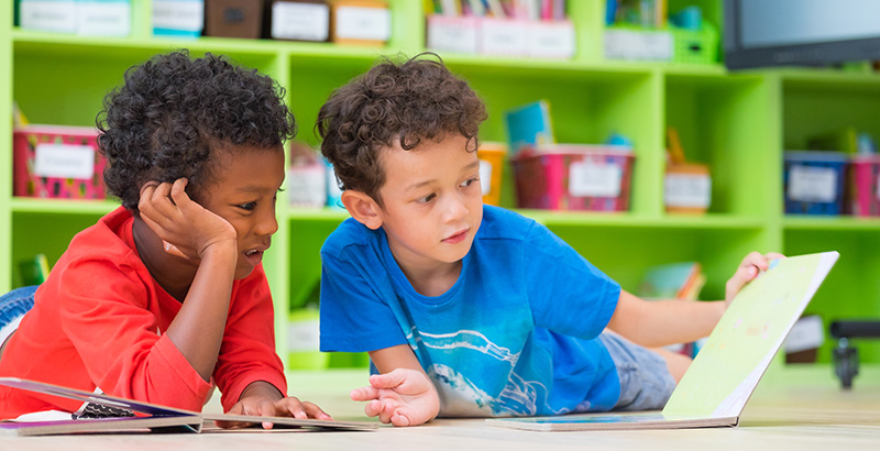 a couple of young boys sitting at a table in a classroom