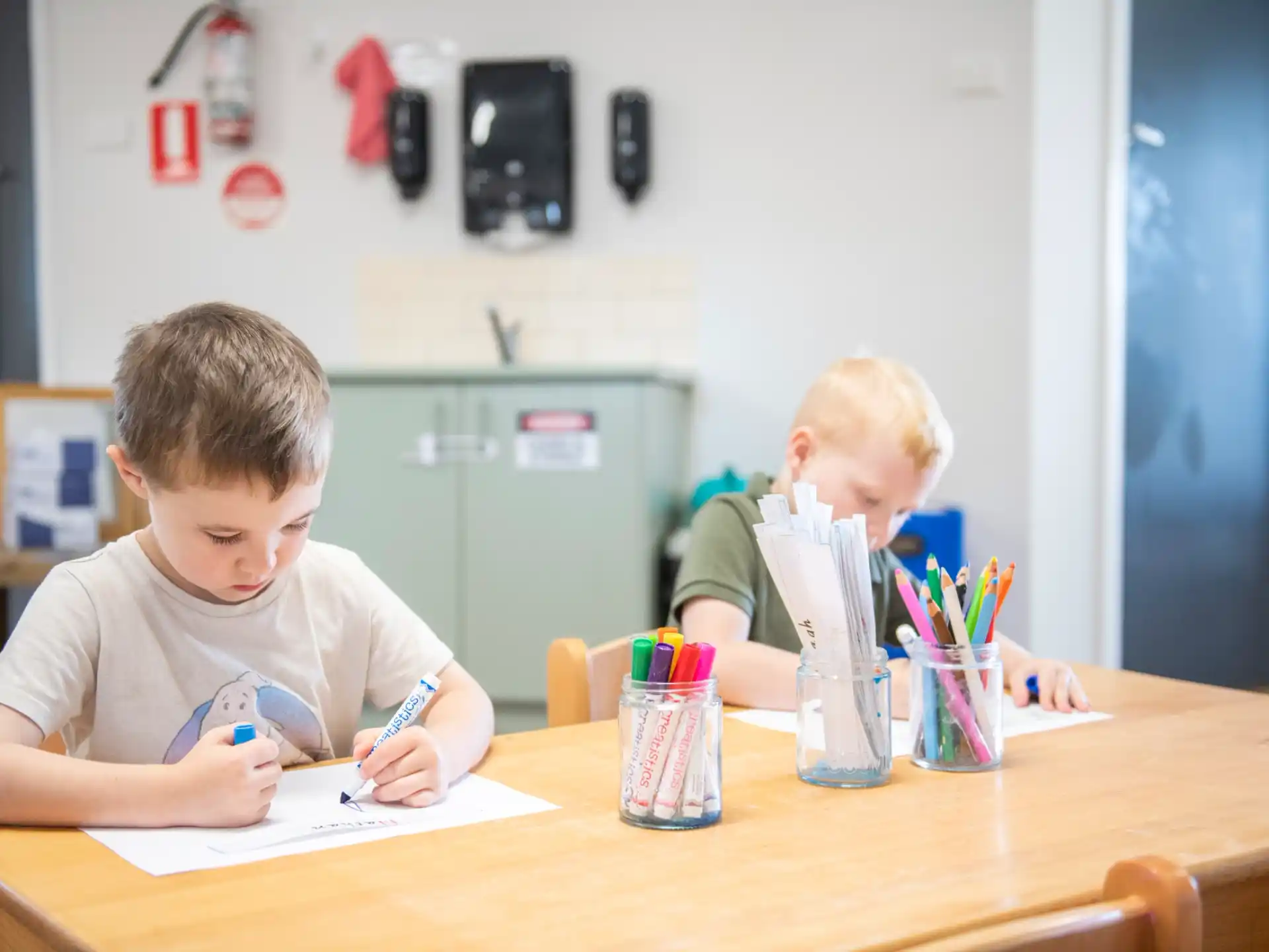 a couple of boys sitting at a table writing on paper