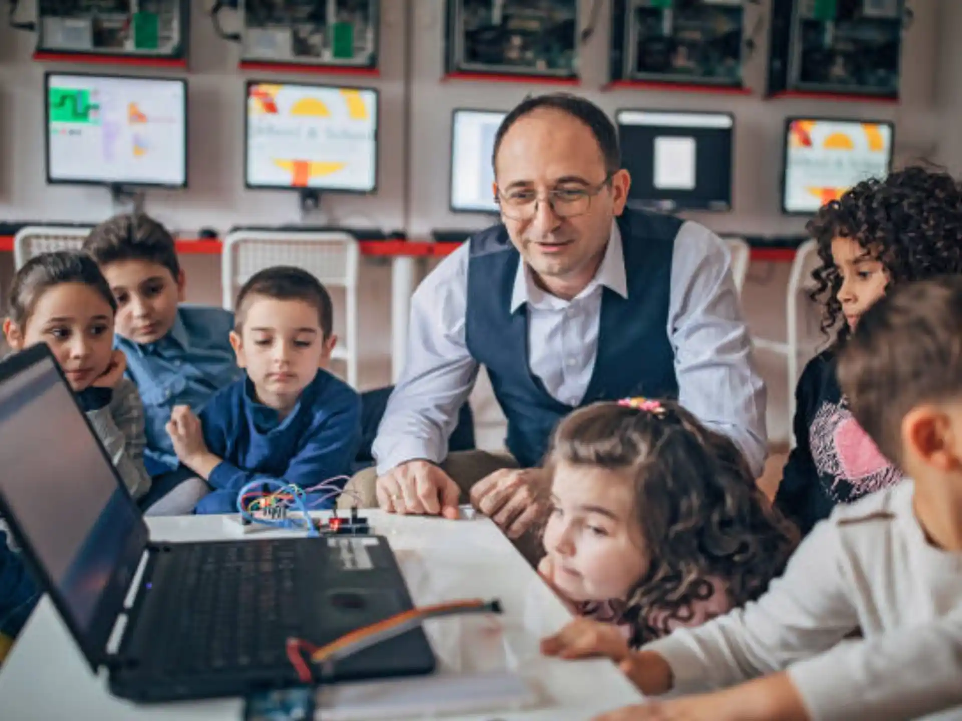 a person showing a group of children something on the laptop