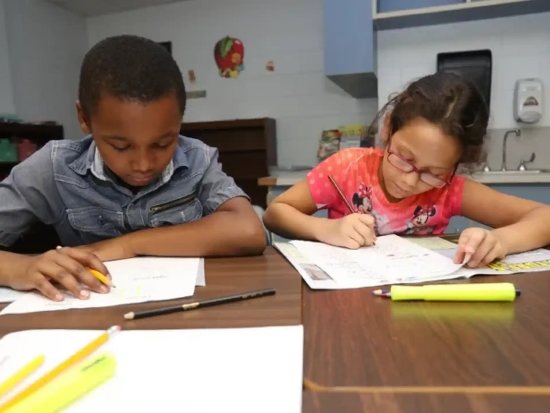 a boy and girl sitting at a table writing on paper