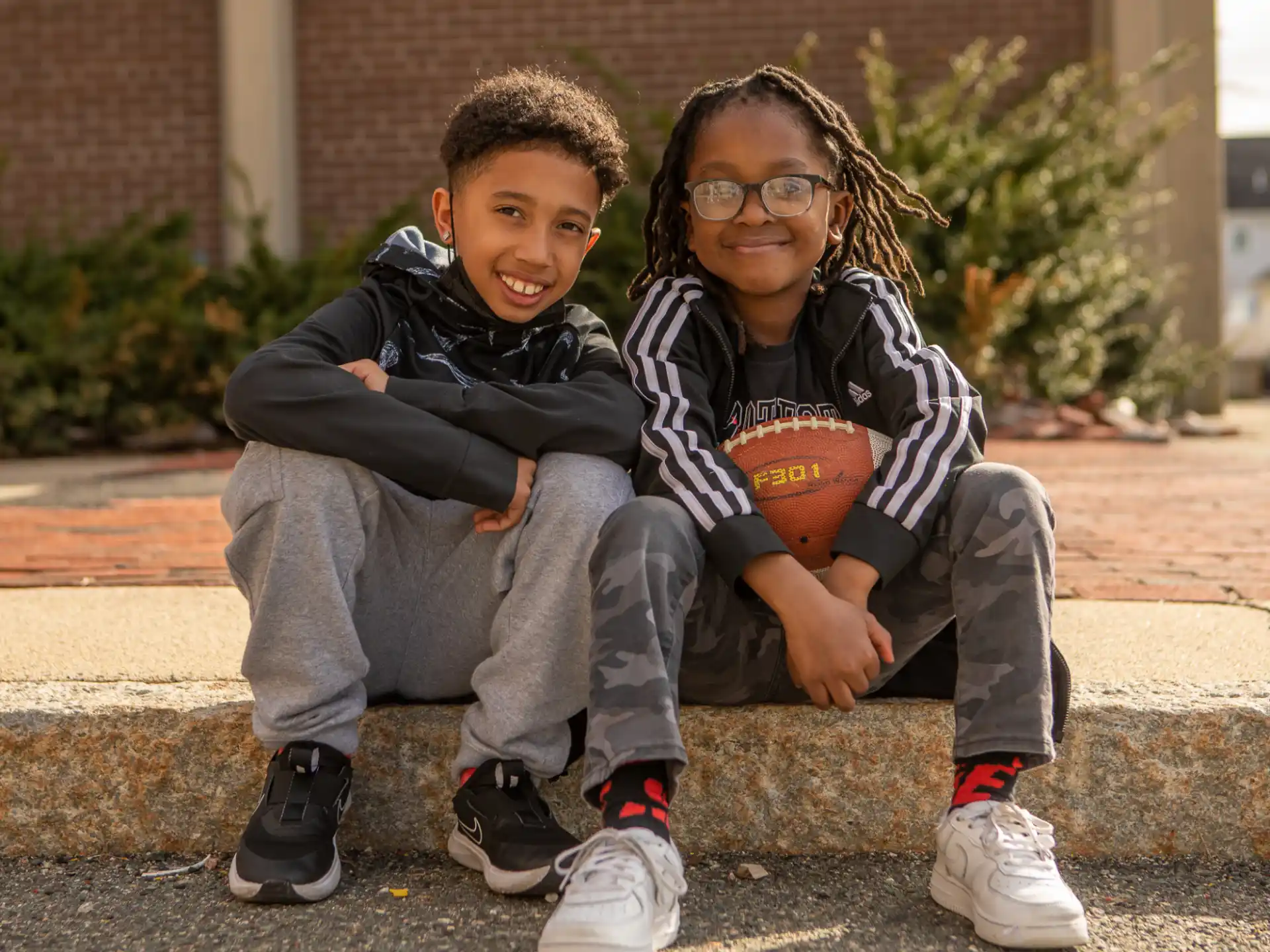 a couple of kids sitting on a stone ledge posing for the camera