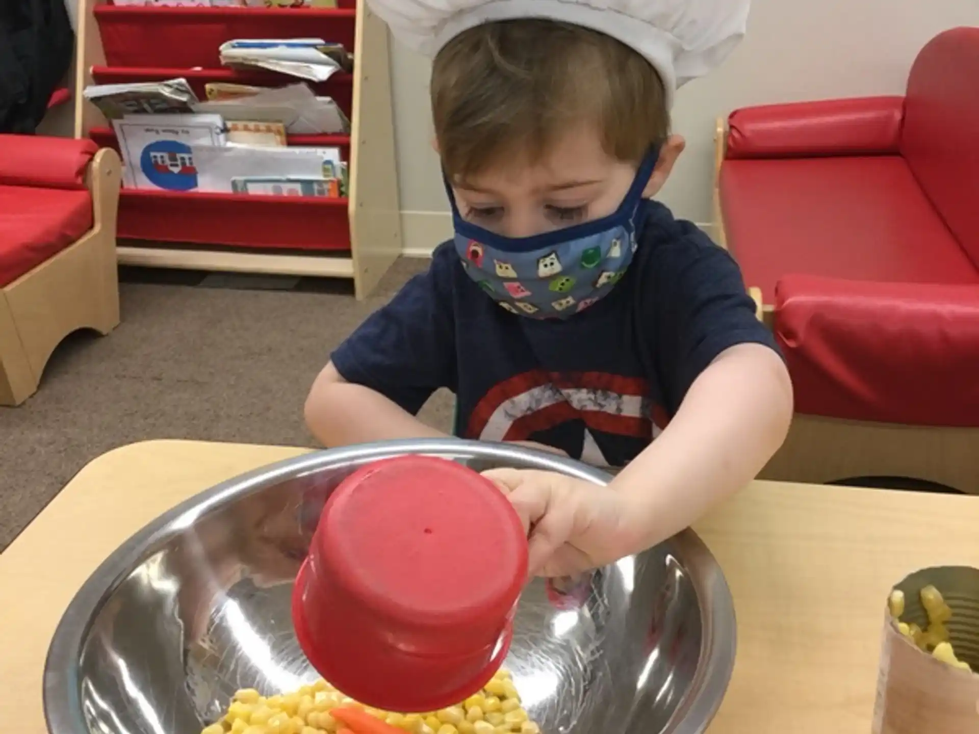 a child in a white hat and blue shirt eating a bowl of food