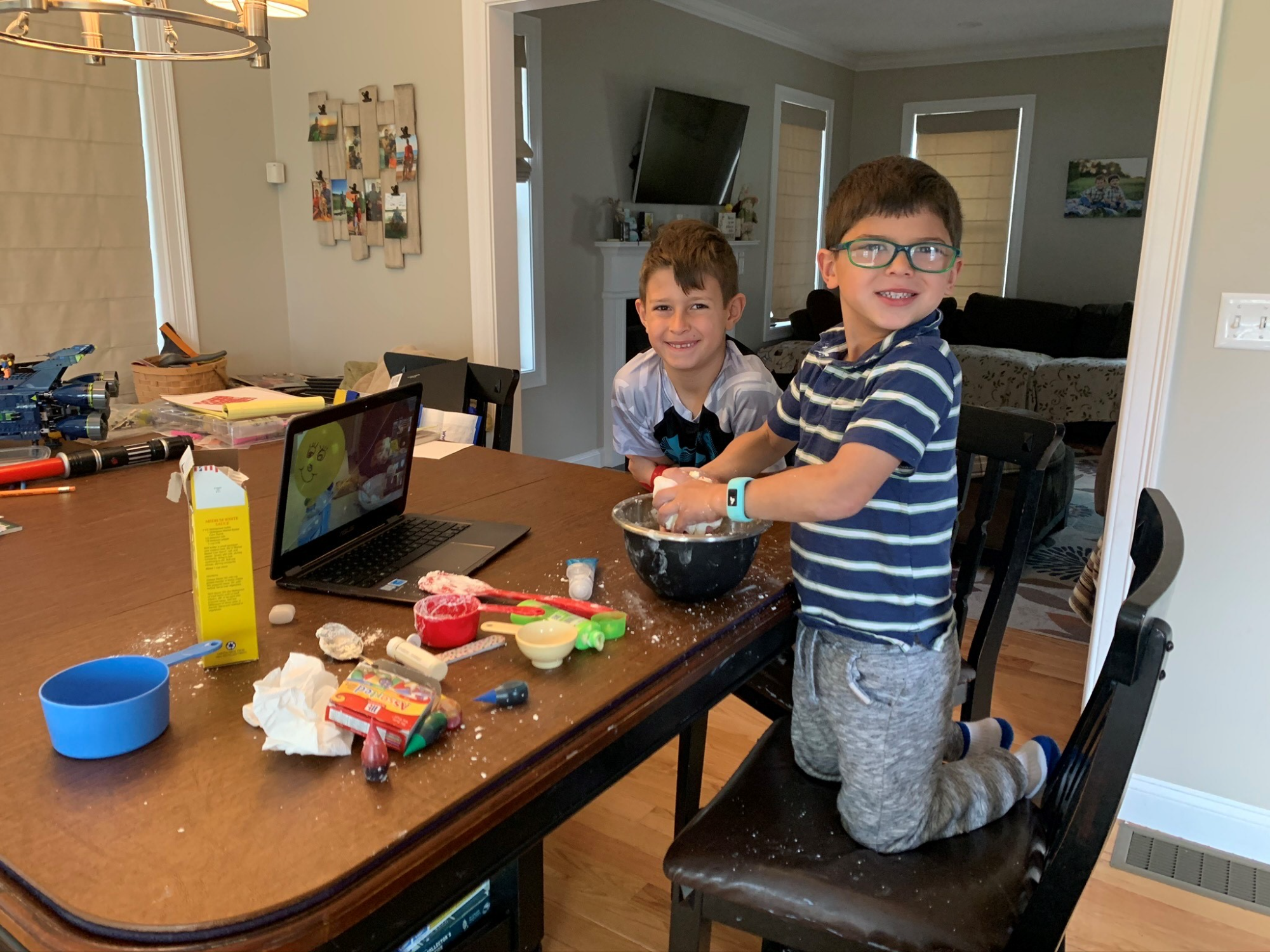 a couple of boys sitting at a table with a laptop and a bowl of food