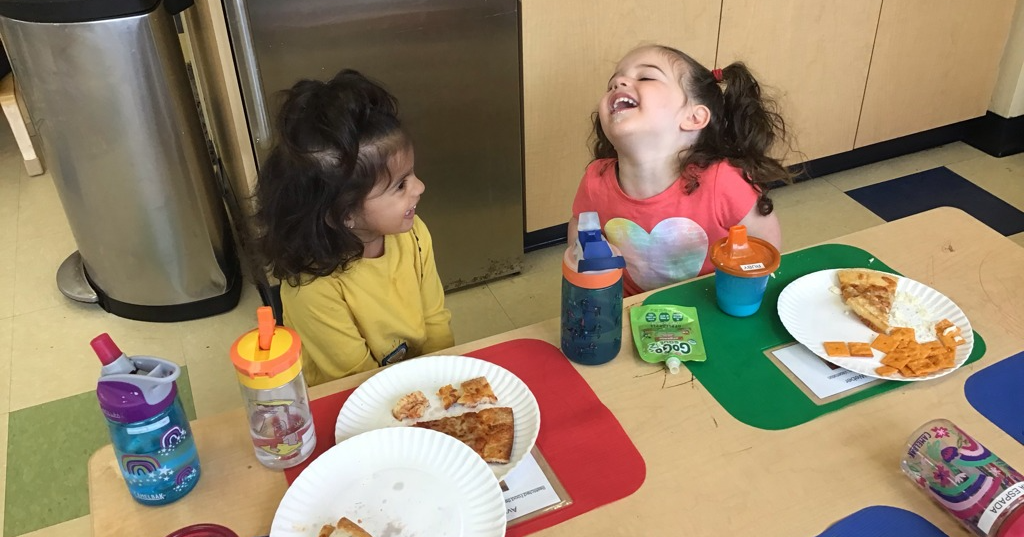a couple of girls sitting at a table with food on it