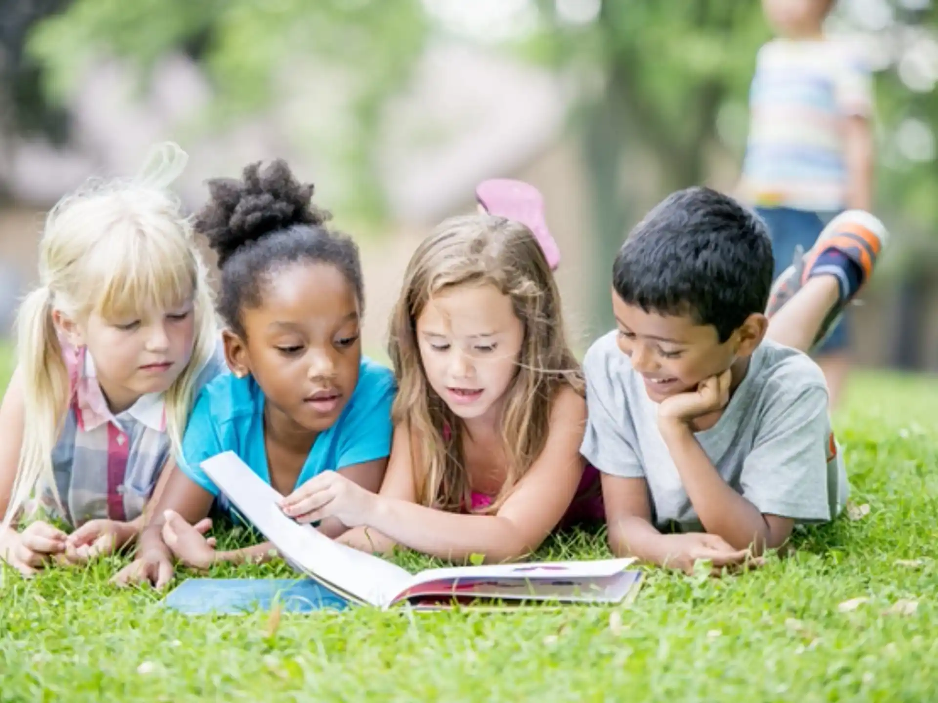 a group of children sitting on the grass looking at a book