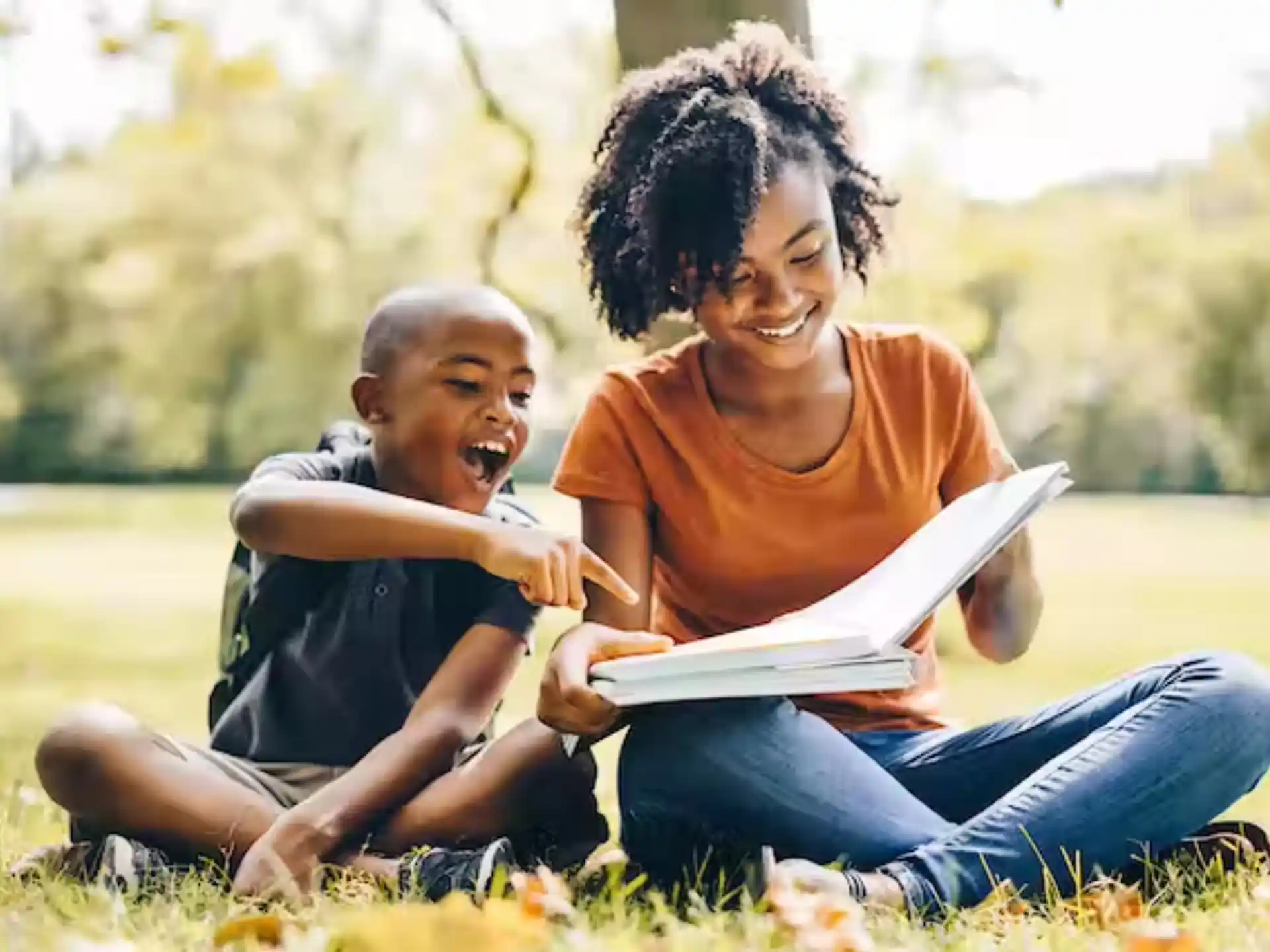a person and a child reading a book in a grassy field