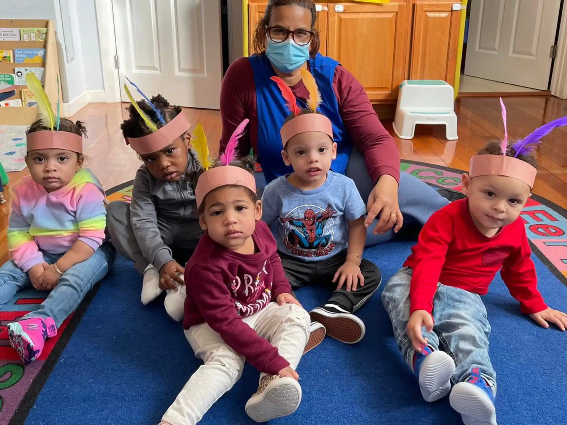 a group of children sitting on the floor with a person in a mask