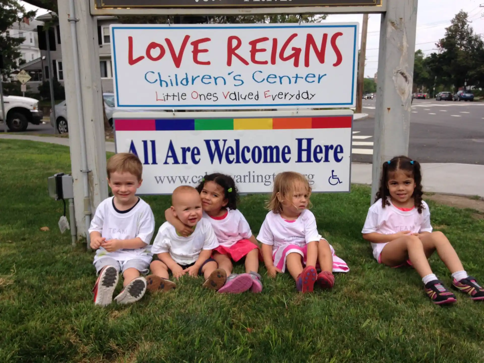 a group of children sitting on grass by a sign