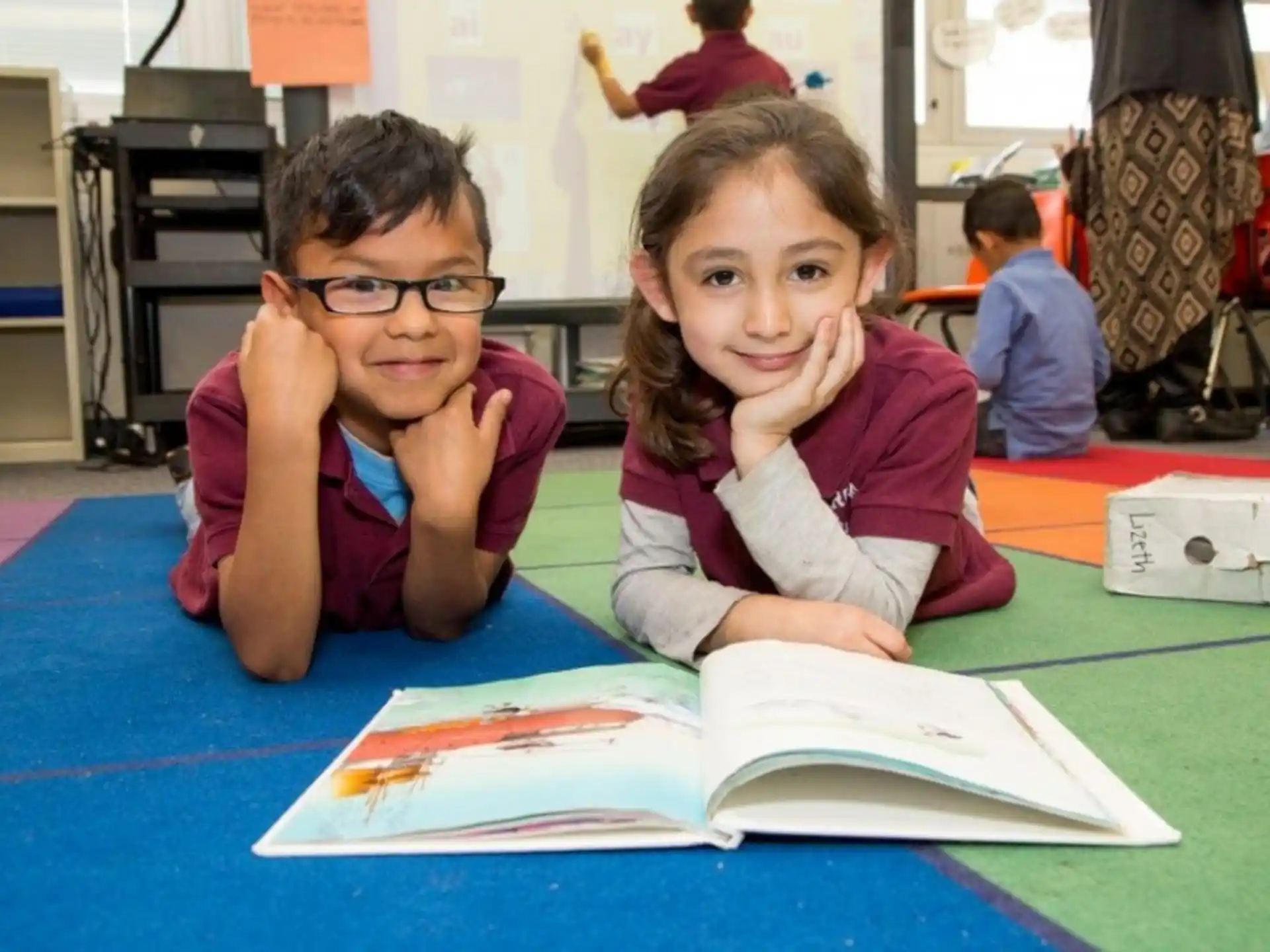 a couple of girls sitting at a table with books and a book