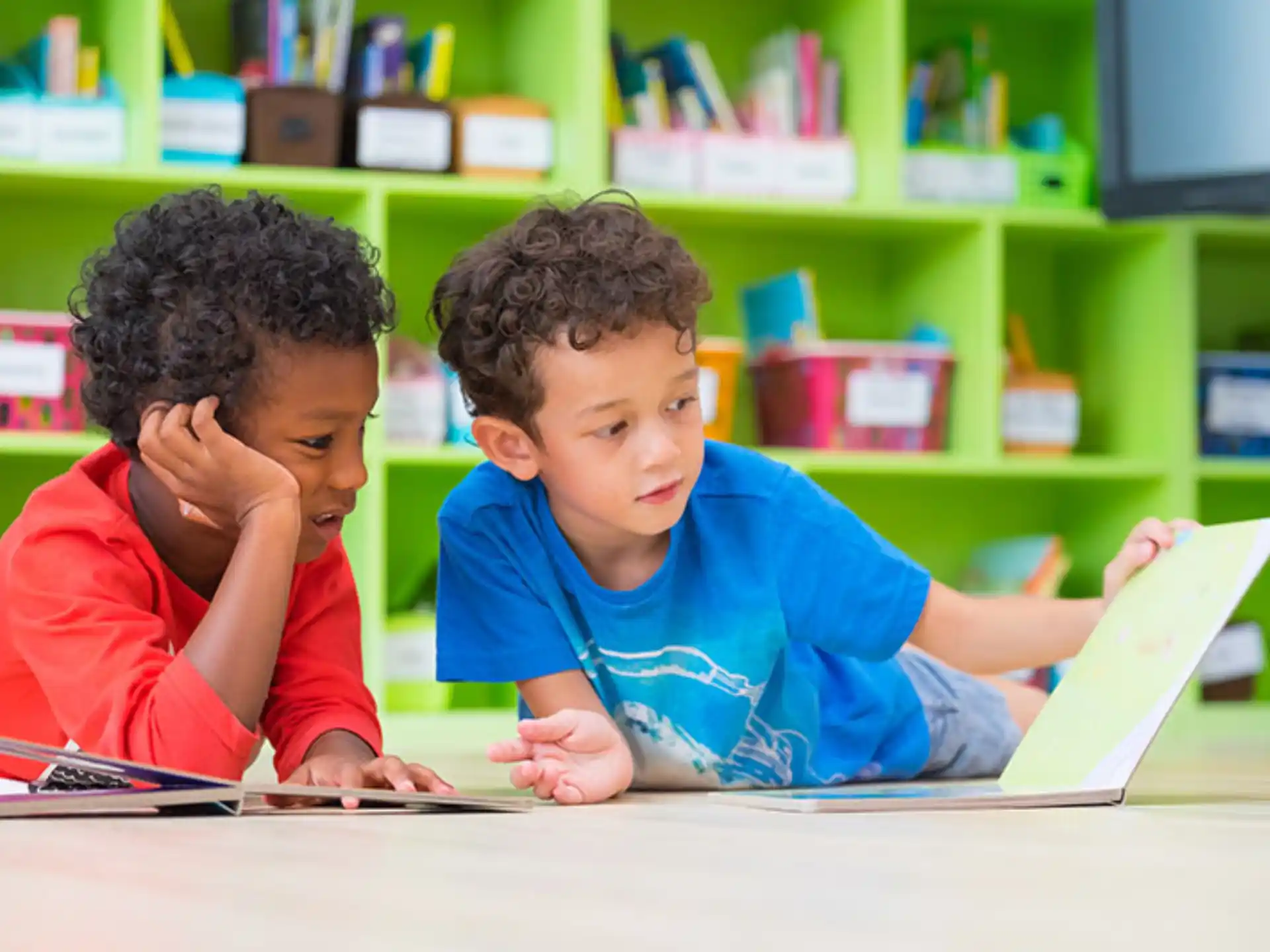 a couple of boys sitting at a table looking at a book
