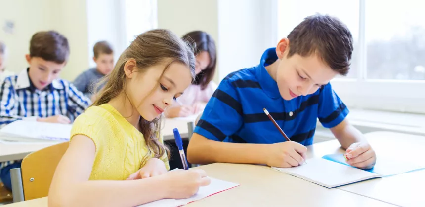 a group of children sitting at a table writing on paper
