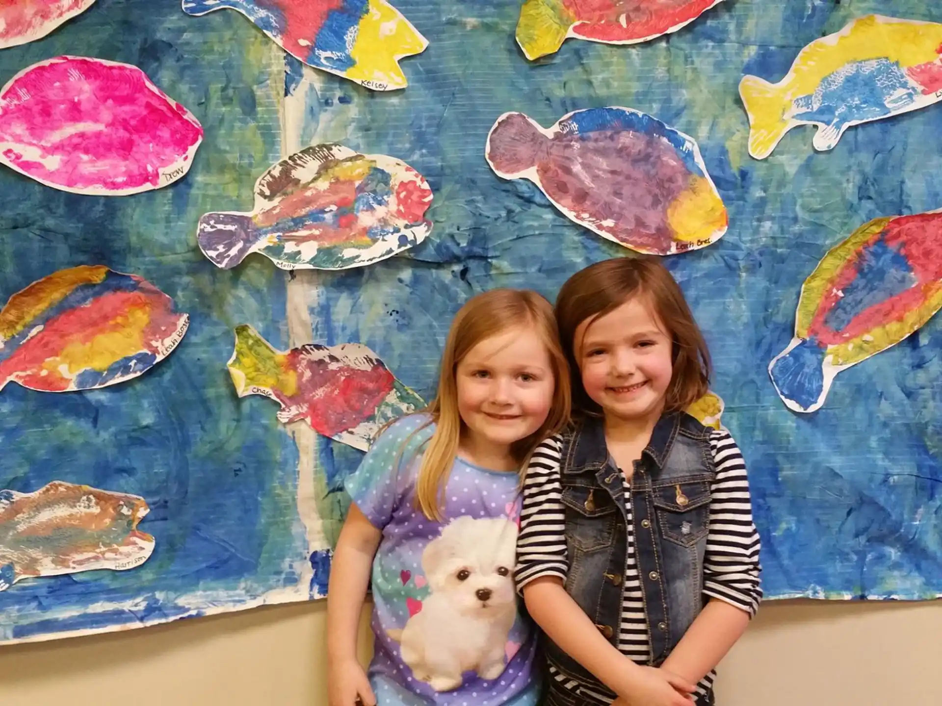 a couple of girls posing for the camera in front of a wall with art