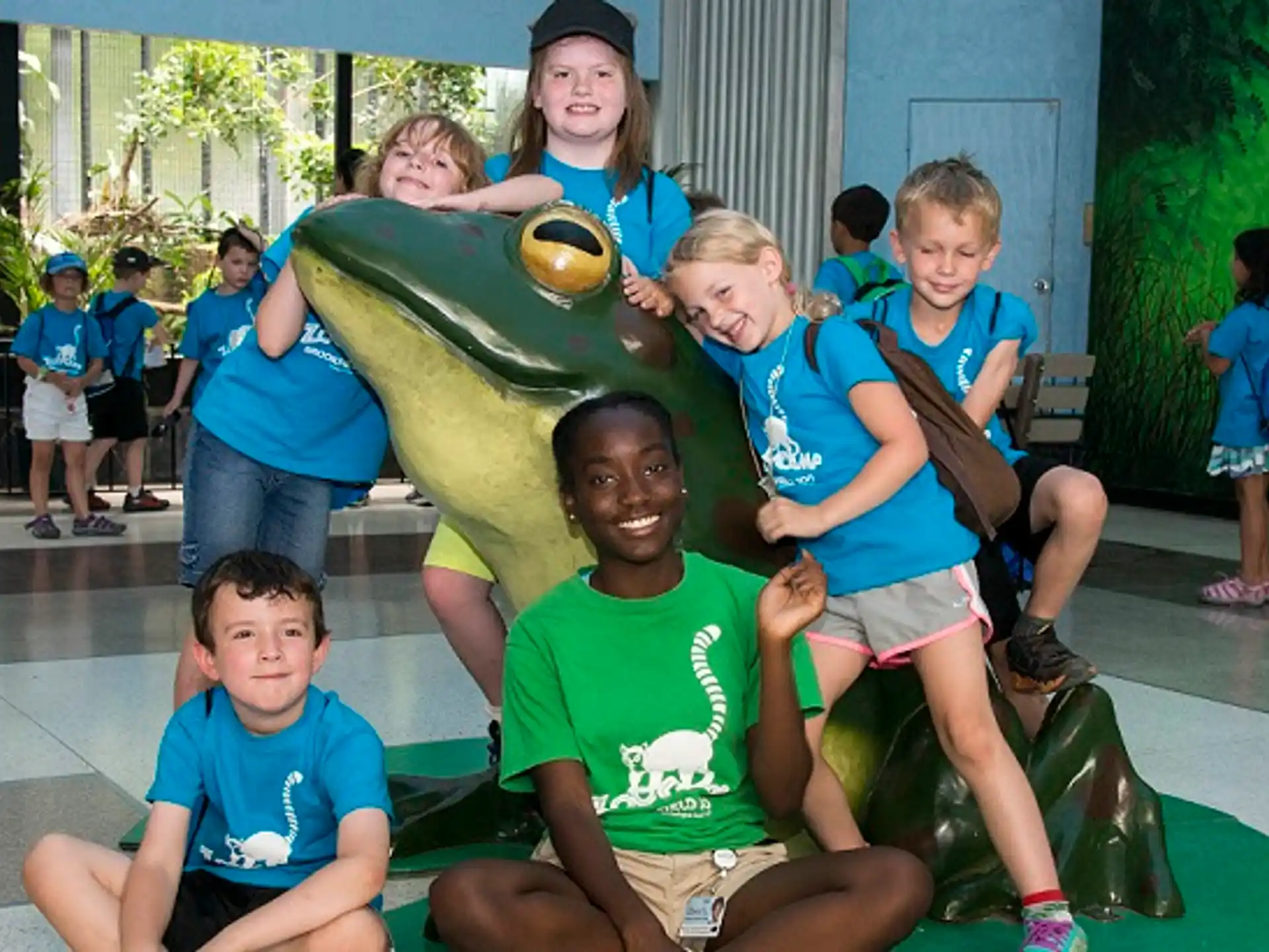 a group of kids posing for a photo in front of a large green frog statue