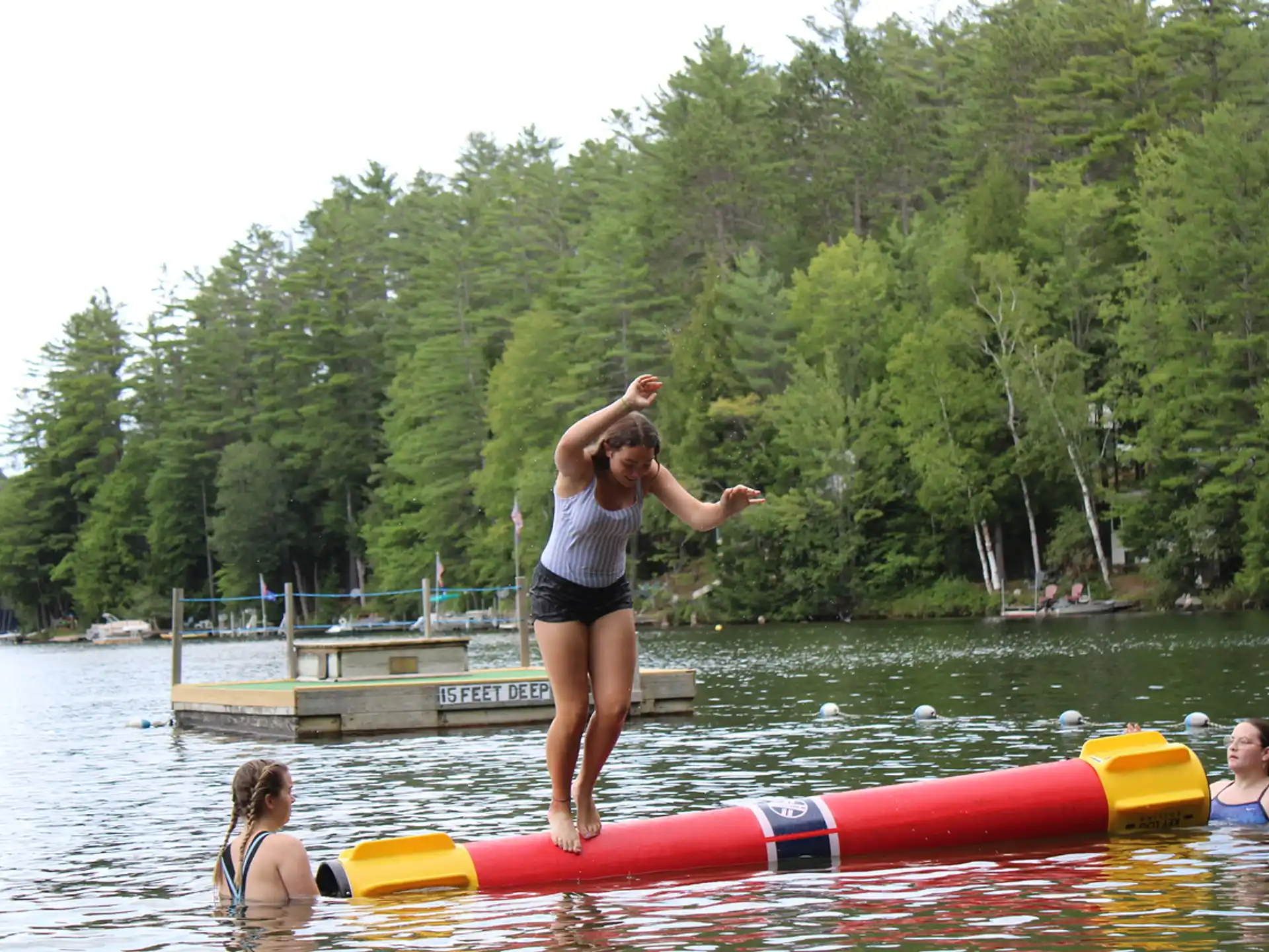 a woman standing on a red kayak in a lake with people in the background