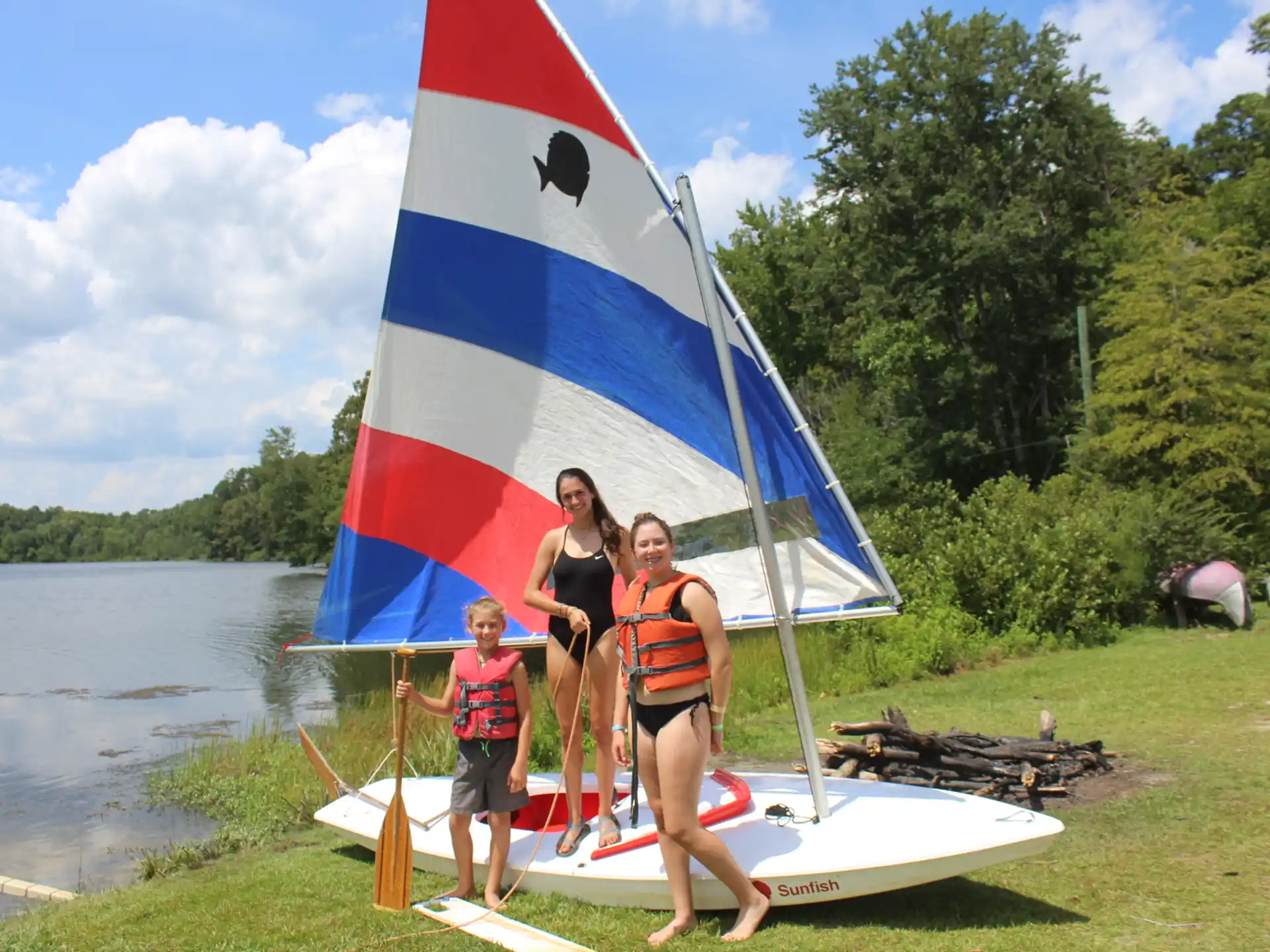 a group of women standing next to a sailboat on a lake