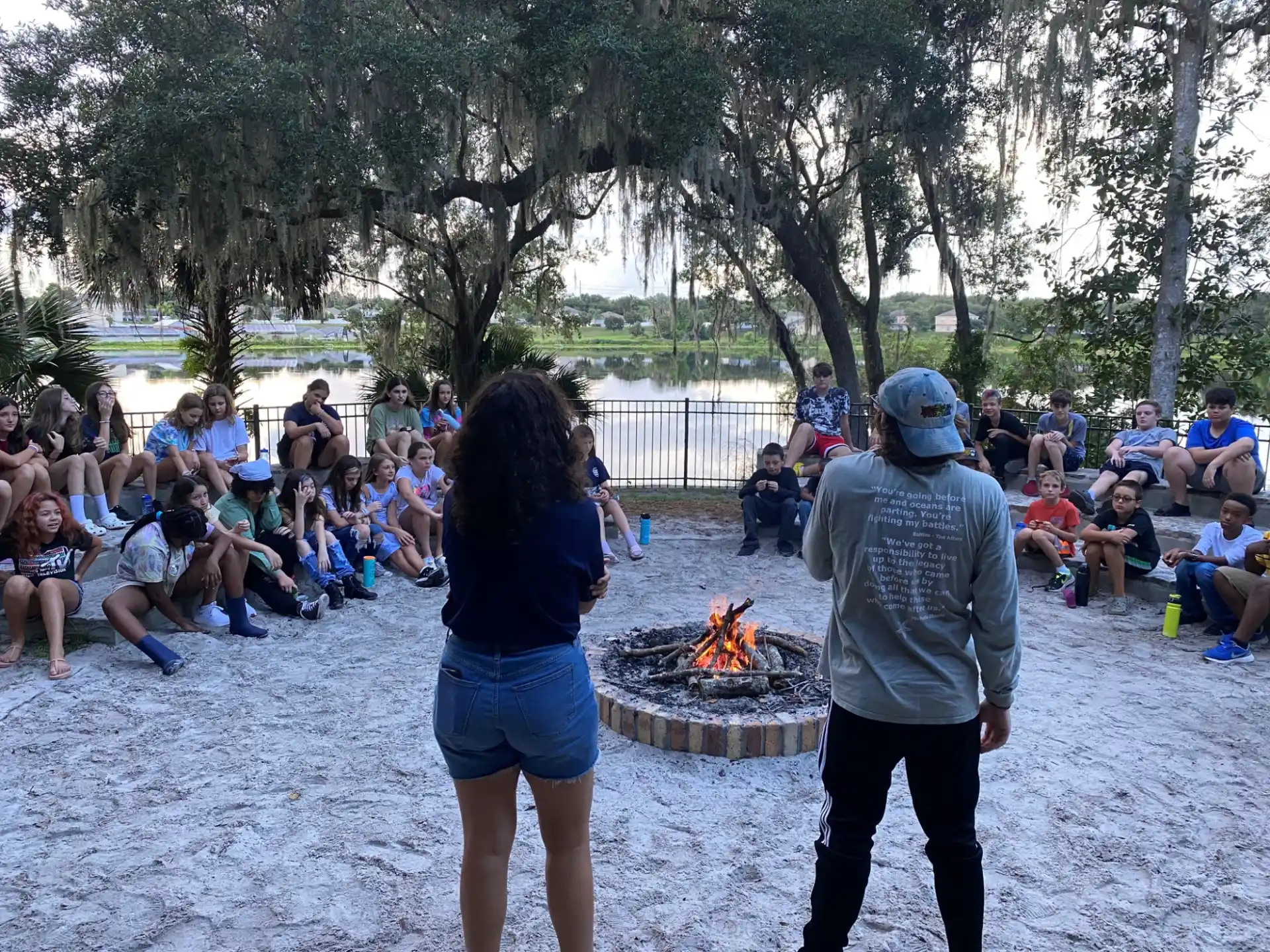 a man and woman standing in front of a fire pit with people sitting around