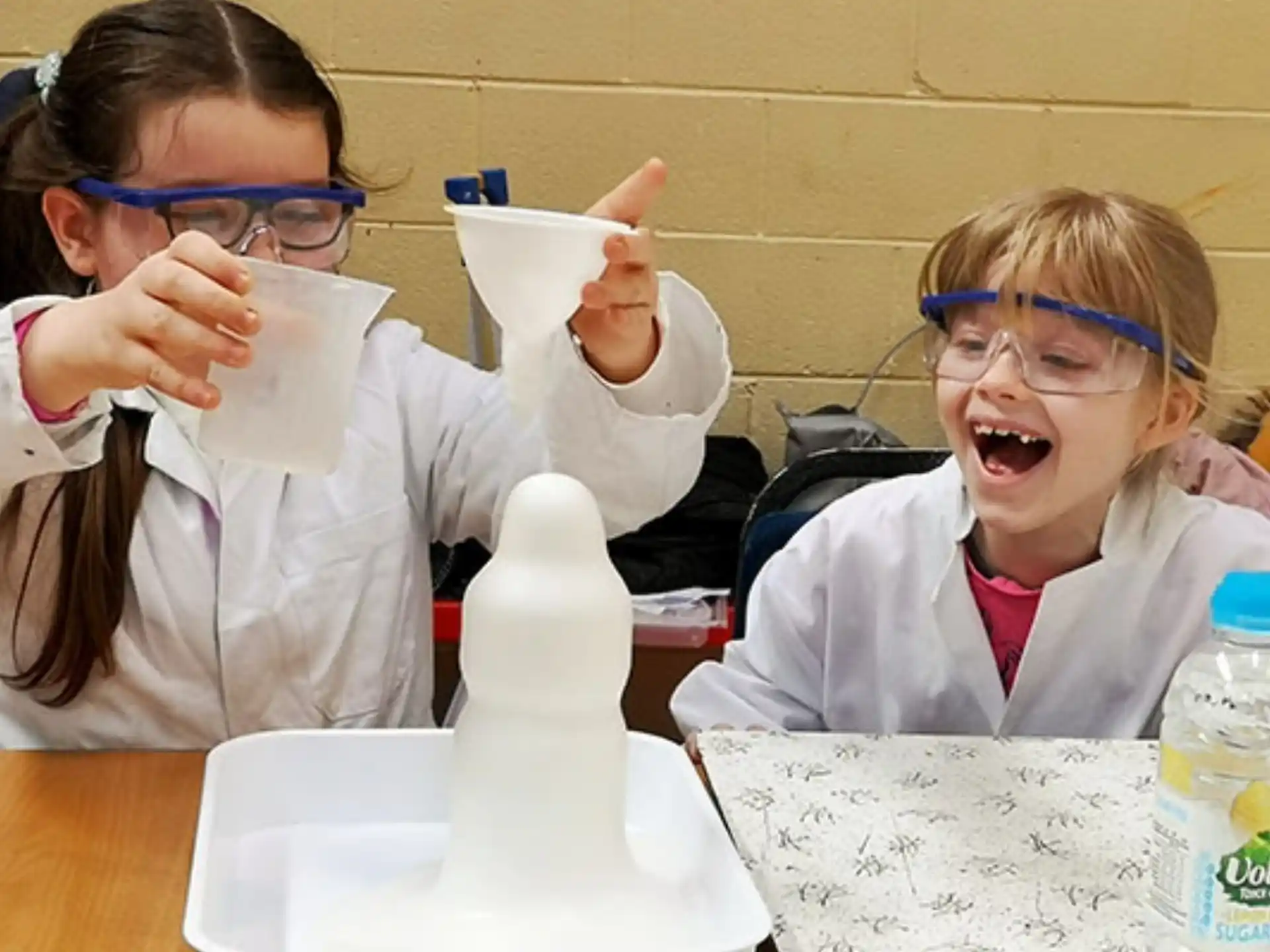 a couple of girls wearing safety goggles and holding up white plastic cups