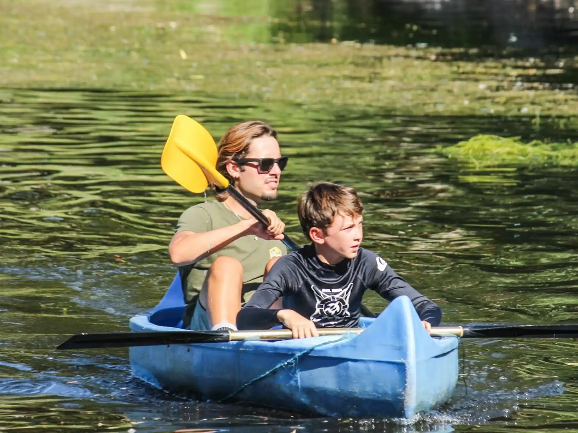 a person and a boy in a small blue boat on water