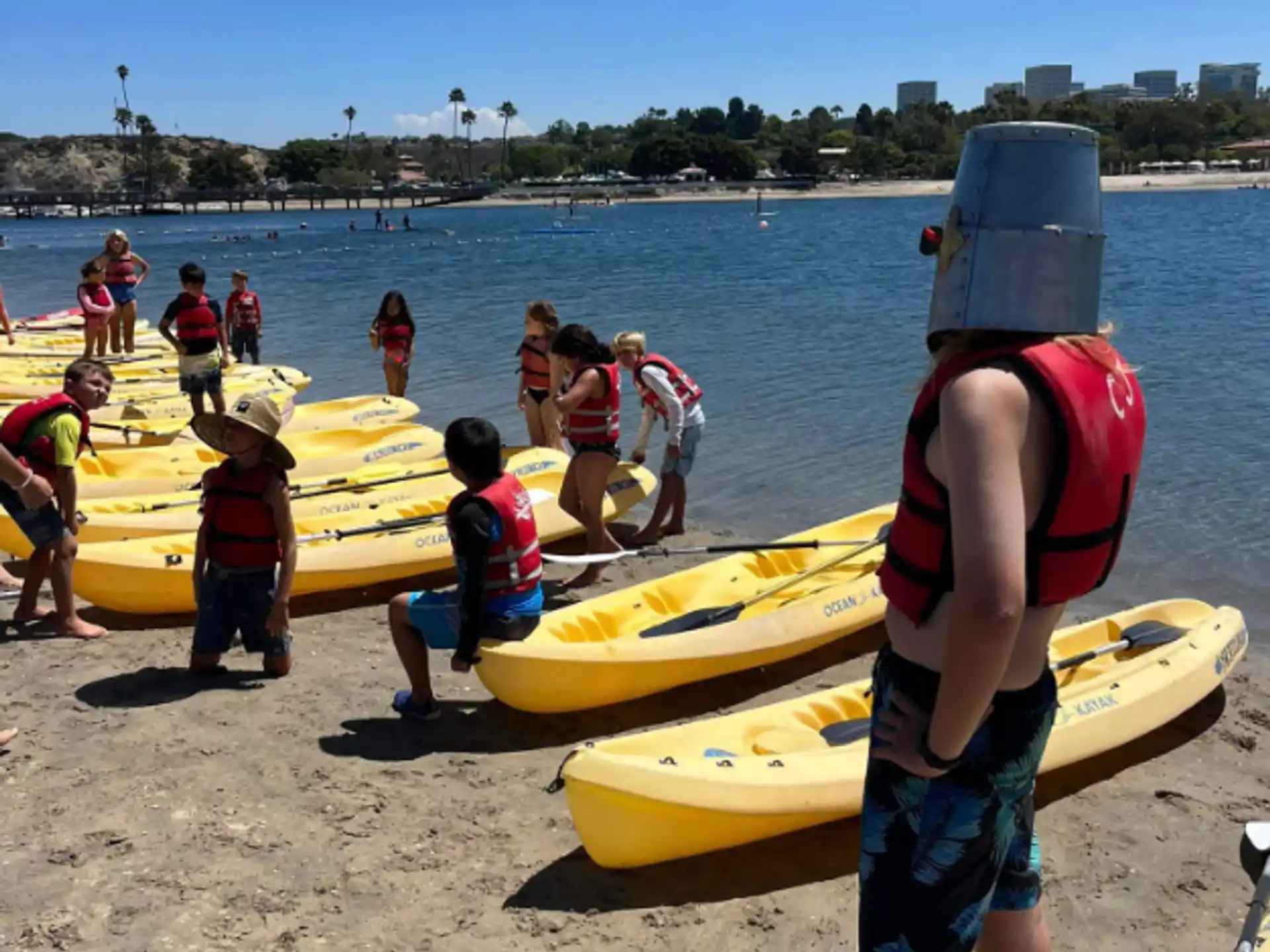 a group of people standing next to yellow kayaks on a beach