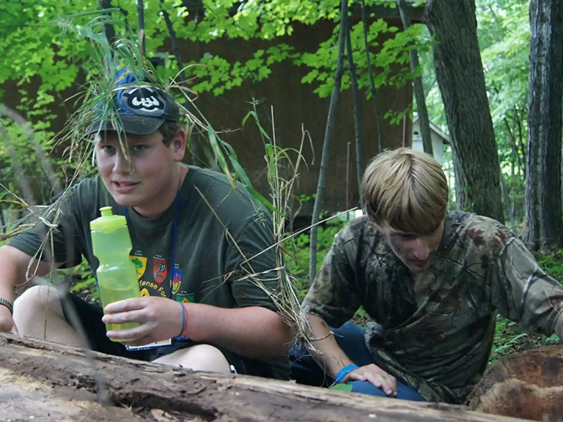 a couple of men in camouflage sitting on a log in the woods