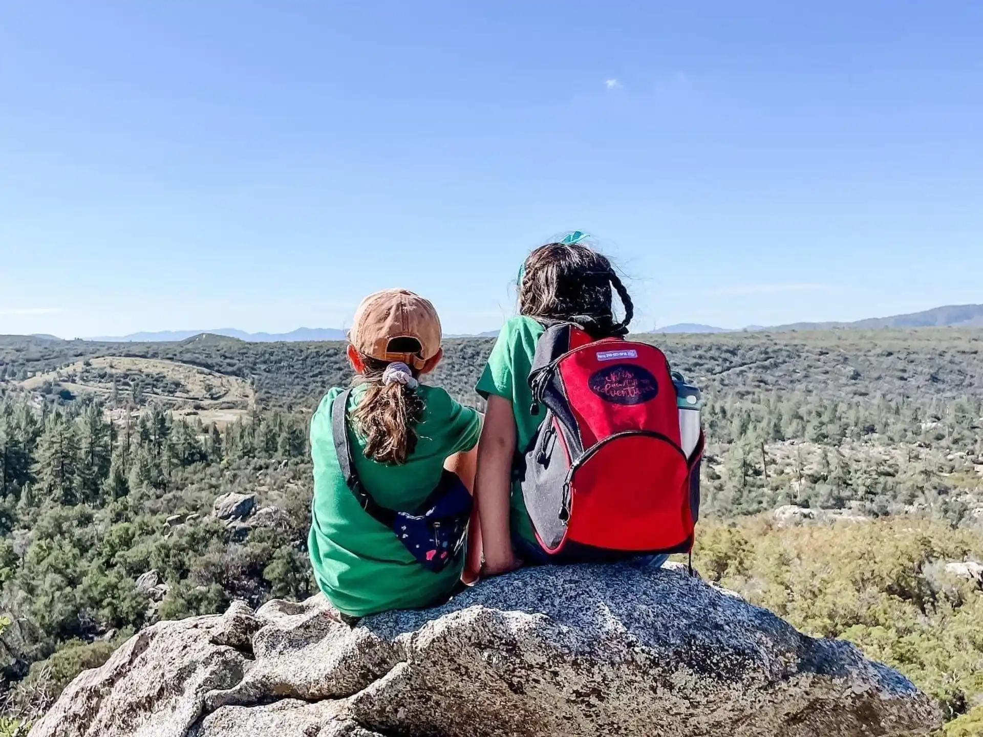 a couple of people sitting on a rock overlooking a valley