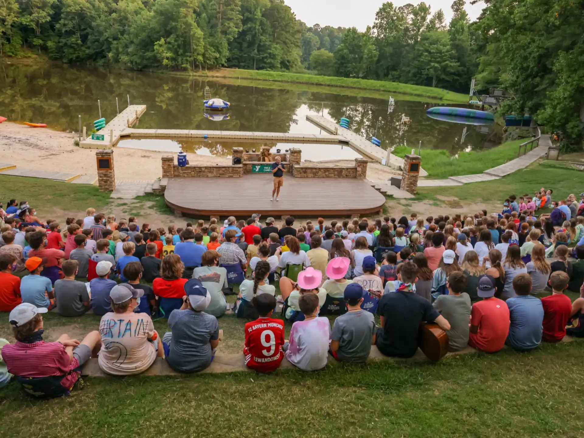 a group of people sitting on the grass looking at a person on a stage
