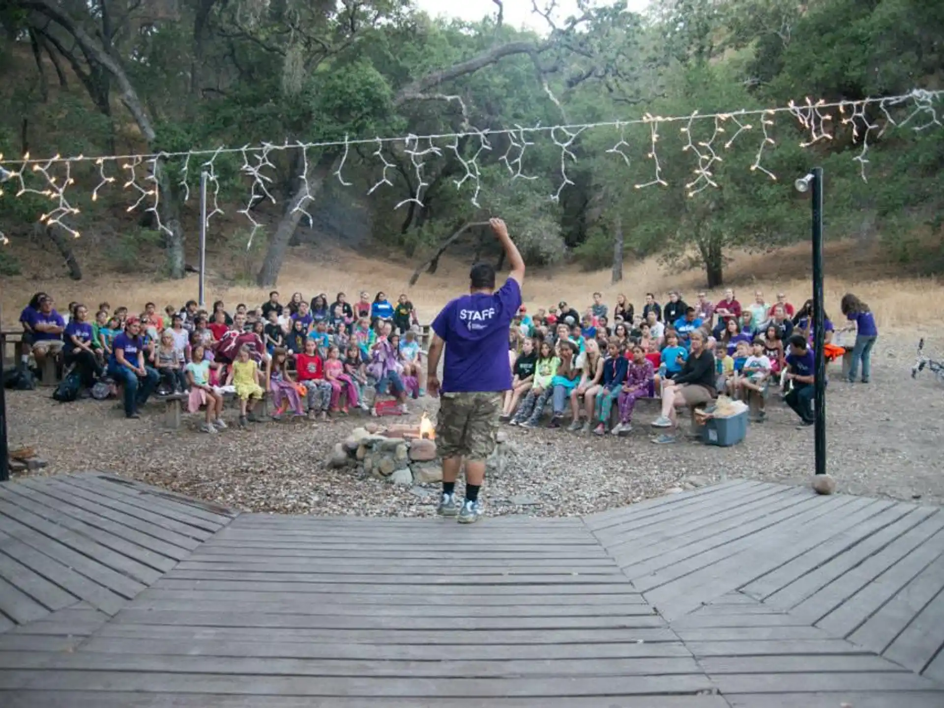 a person standing on a deck with a group of people sitting on the ground