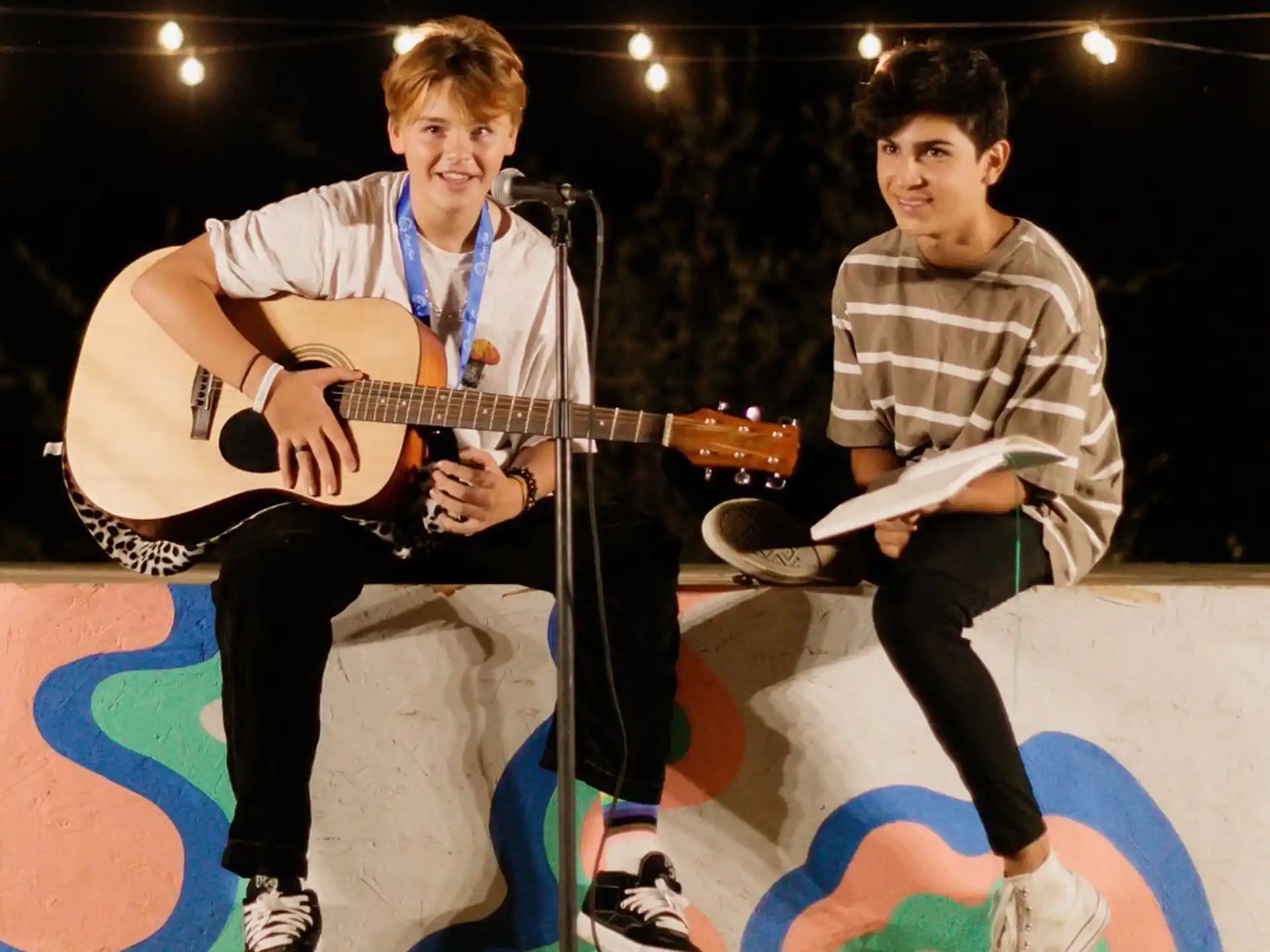 a couple of boys sitting on a stage with a guitar