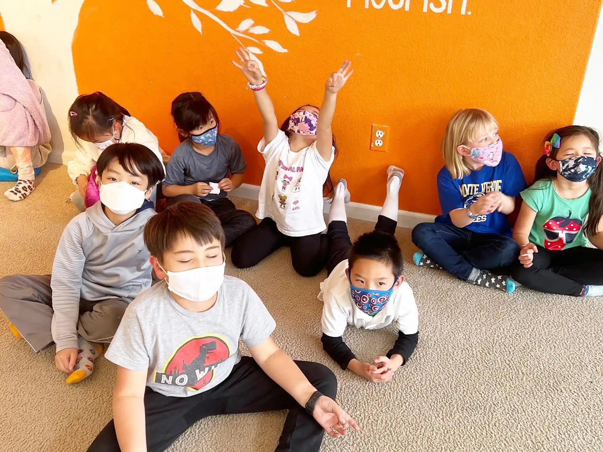 a group of children sitting on the floor with their hands up