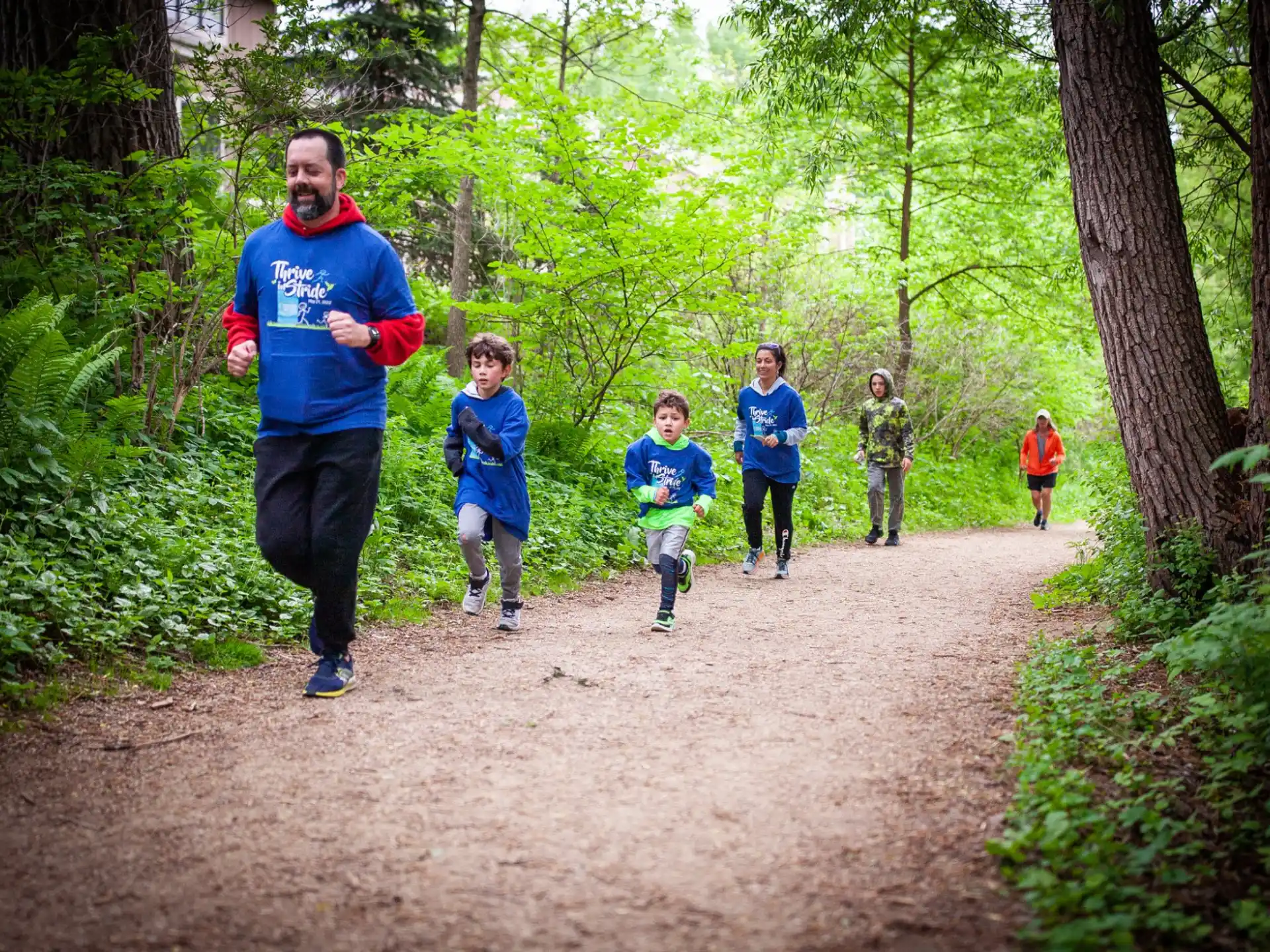 a group of people running on a dirt path in the woods