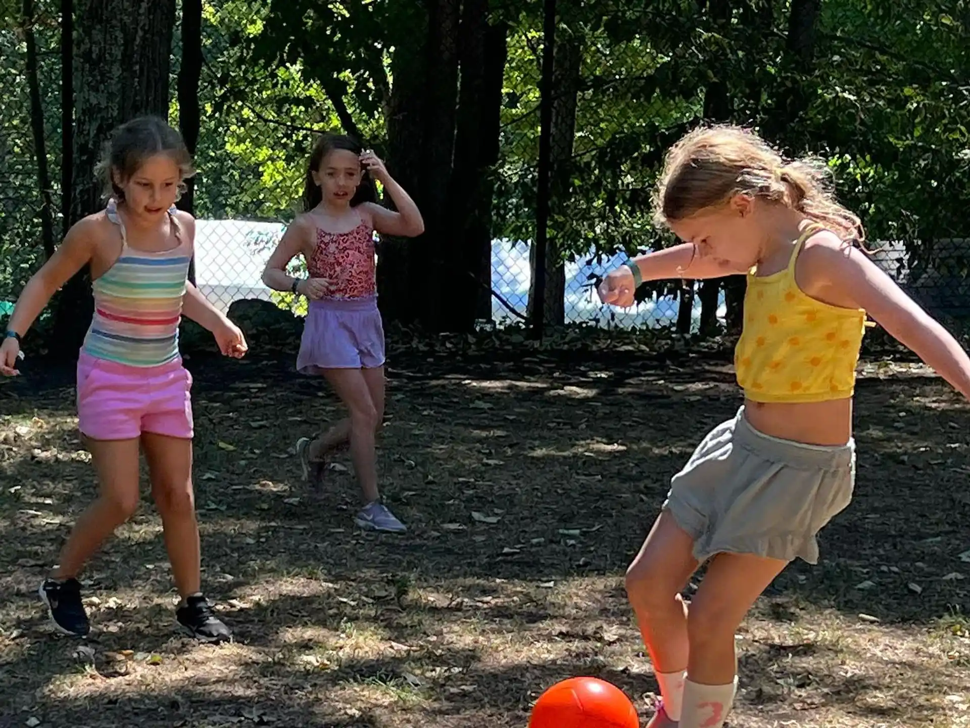 a group of girls playing with a ball in a wooded area